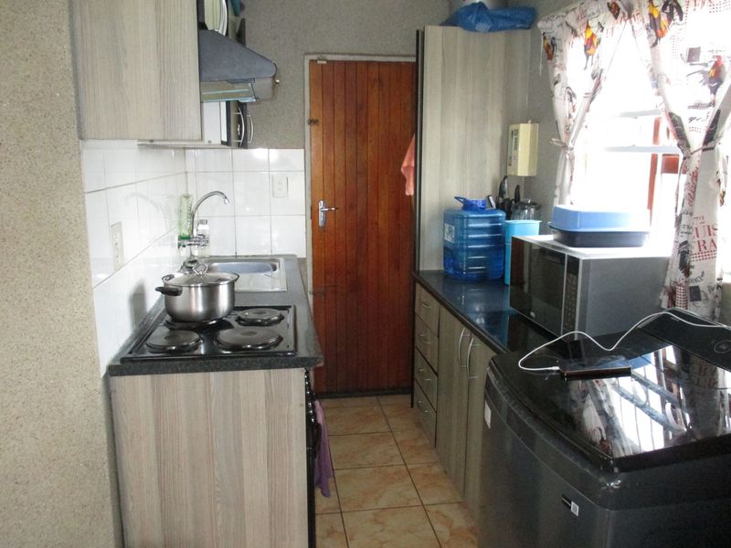 Compact kitchen featuring laminate cabinetry, granite countertops, electric hob, extractor fan, and tiled backsplash with direct access to an exterior timber door.