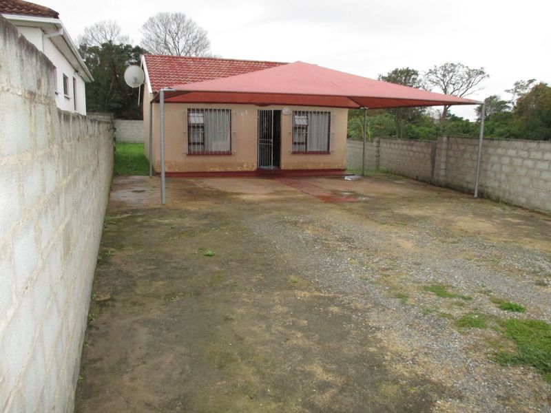 Front view of a detached house featuring a shade sail carport, security bars on windows, and a concrete boundary wall.