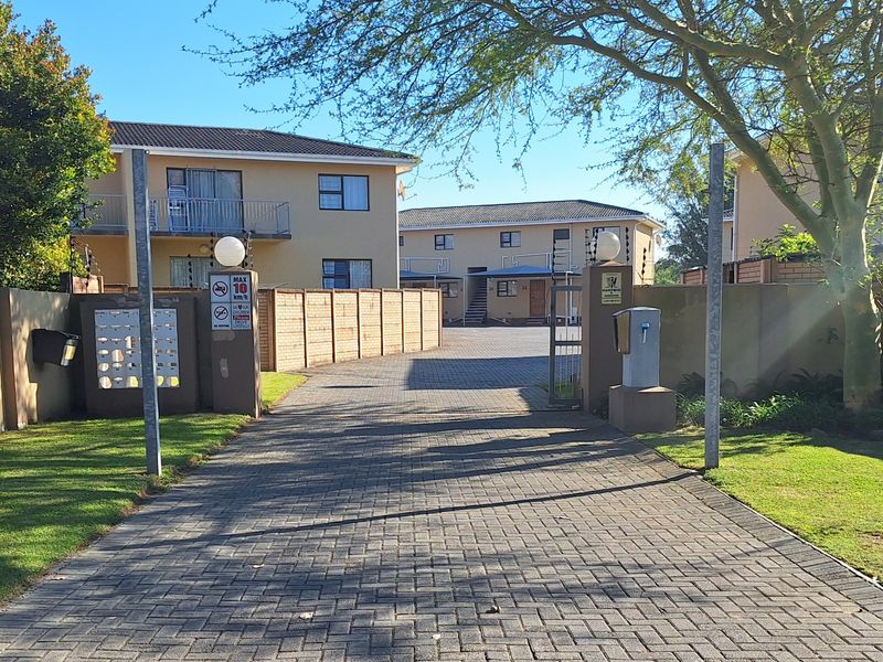 A paved driveway entrance to an apartment complex featuring perimeter walls, electric fencing, security gate, and a bank of post boxes.