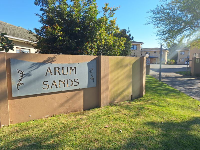Entrance view of Arum Sands apartment complex featuring a boundary wall with electric fencing and paved driveway access.