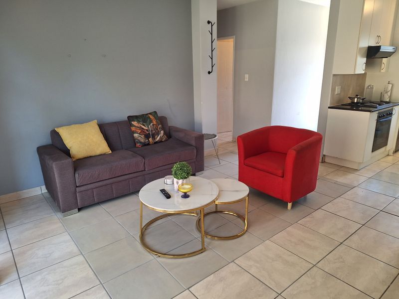 Open-plan living area featuring tiled flooring and a compact kitchen with built-in oven, hob, and extractor fan.