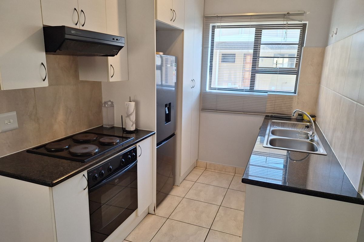 A functional kitchen featuring white cabinetry, dark countertops, an electric hob with extractor, and a double sink with tiled flooring and backsplash.