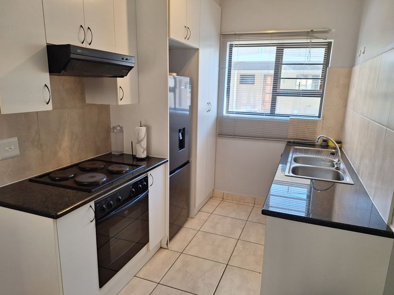 A functional kitchen featuring white cabinetry, dark countertops, an electric hob with extractor, and a double sink with tiled flooring and backsplash.