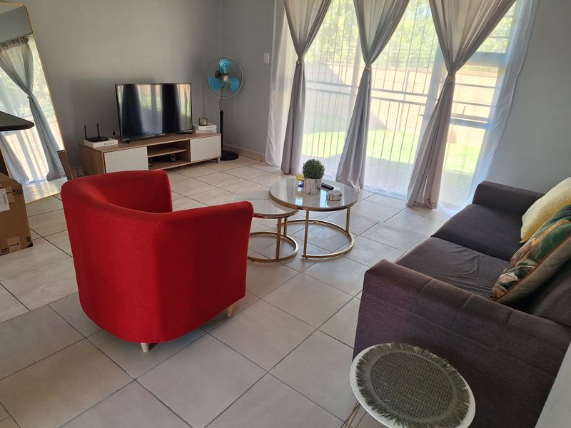 A bright living room featuring neutral tiled flooring and a large sliding glass door with a security gate, providing access to the outdoor area.
