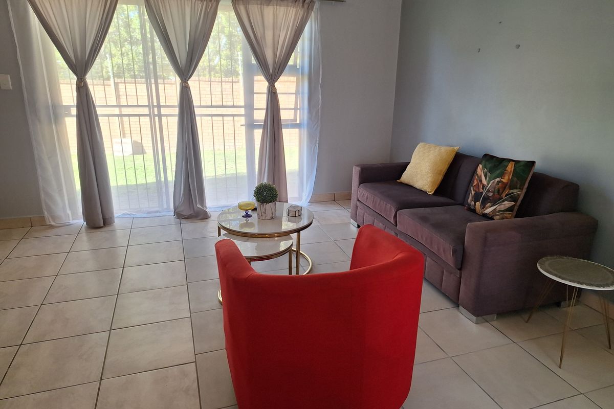 A living room featuring neutral tiled flooring and a large sliding glass door that provides access to the outdoor area.