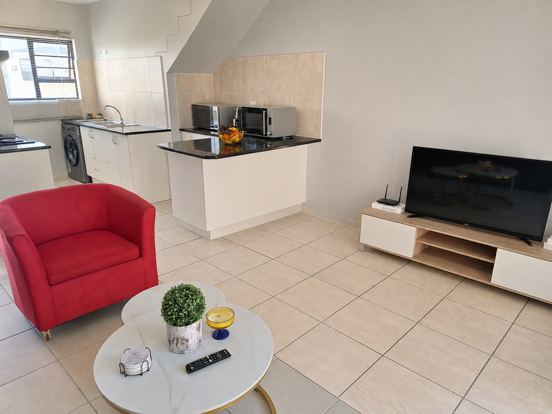 An open-plan living and kitchen area featuring tiled flooring, modern cabinetry with granite countertops, and a functional layout under a staircase.