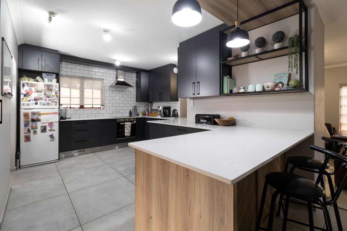 Modern kitchen featuring dark cabinetry, white quartz countertops, subway tile backsplash, and a functional island with integrated breakfast bar seating.