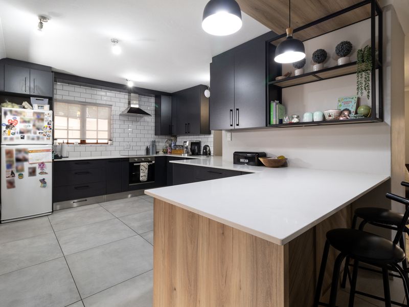 Modern kitchen featuring dark cabinetry, white quartz countertops, subway tile backsplash, and a functional island with integrated breakfast bar seating.