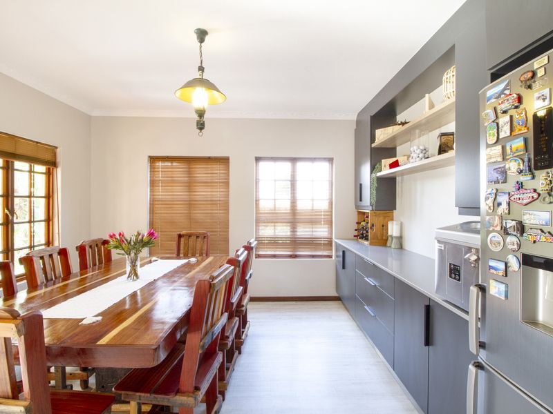 A bright dining room featuring modern dark grey built-in cabinetry, open shelving, and large windows with wooden venetian blinds.