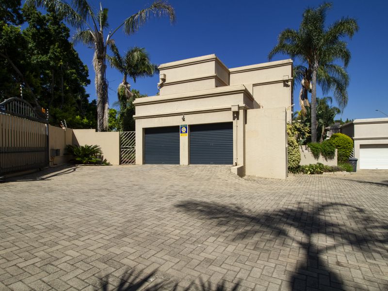 Front exterior view of the property featuring a paved driveway, double garage with roller doors, and secure boundary walling with electric fencing.