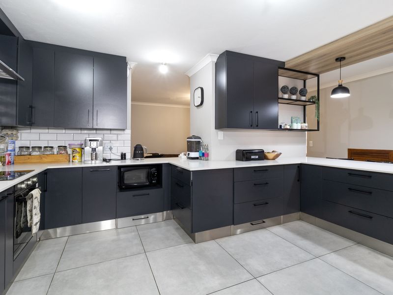 Modern kitchen featuring dark cabinetry, white quartz countertops, subway tile backsplash, built-in appliances, and contemporary pendant lighting.