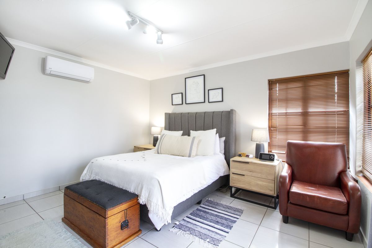 A well-maintained bedroom featuring tiled flooring, an air conditioning unit, track lighting, and wooden blinds, offering a comfortable and functional living space.