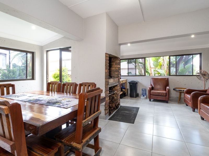 Open-plan living and dining area featuring a built-in brick fireplace, tiled flooring, and large windows providing natural light and garden views.