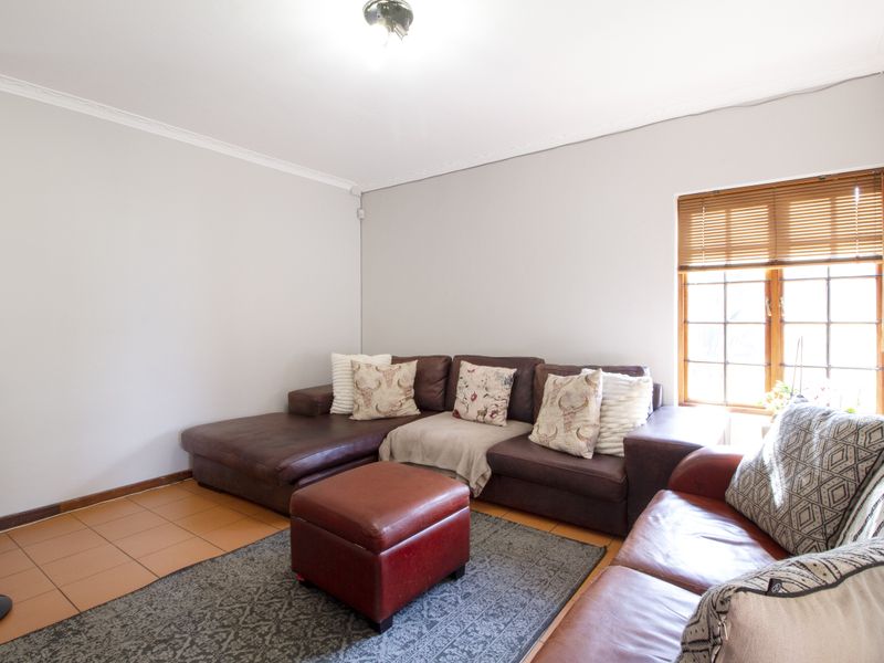 A comfortable living room featuring tiled flooring, cornicing, and natural light through wooden-framed windows with fitted venetian blinds.
