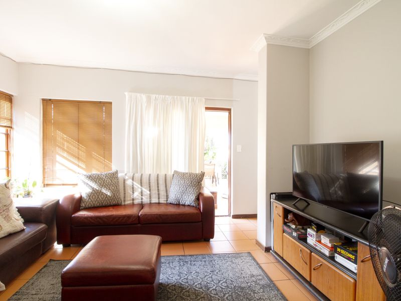 A comfortable living room featuring tiled flooring, classic cornicing, and natural light through wooden window frames, with direct access to an outdoor patio area.