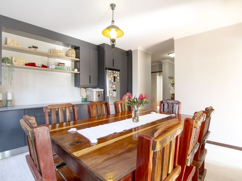 A well-lit dining area featuring modern dark grey built-in cabinetry with open shelving and a classic pendant light fixture.