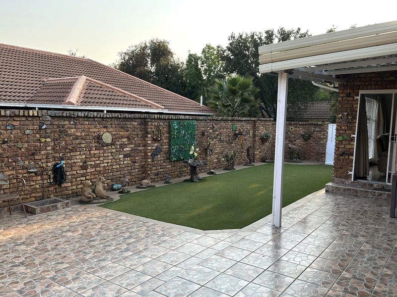 A private rear courtyard featuring a tiled patio area, covered veranda, and a low-maintenance artificial lawn enclosed by a brick boundary wall.