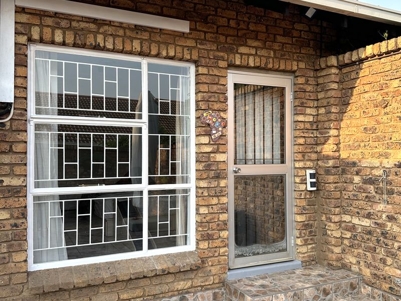 A paved patio area featuring face brick walls, a security gate, and windows with fitted security bars.