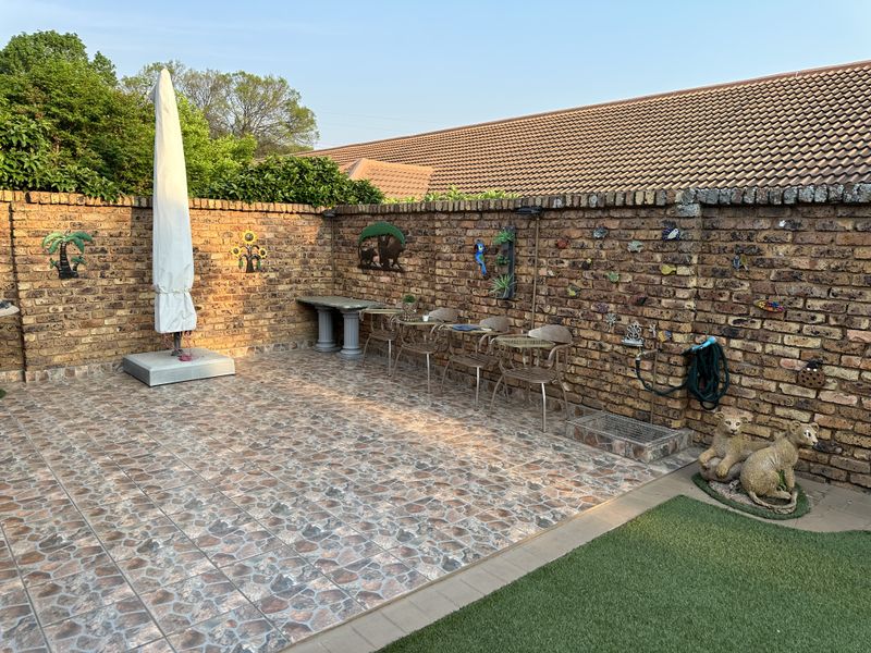 A paved outdoor patio area featuring a brick boundary wall, artificial grass section, and an integrated water tap, suitable for outdoor relaxation.