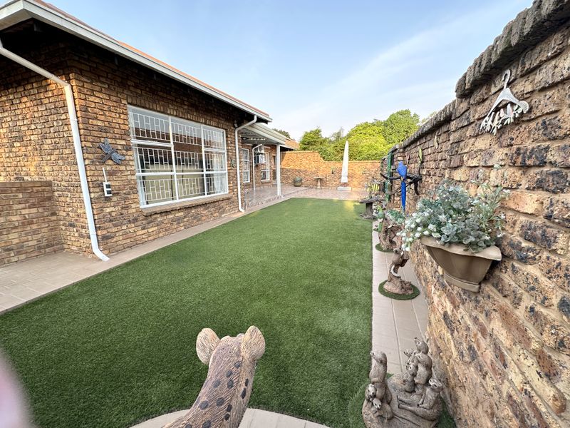 A well-maintained rear garden area featuring a face brick townhouse exterior, artificial lawn, and paved patio space.