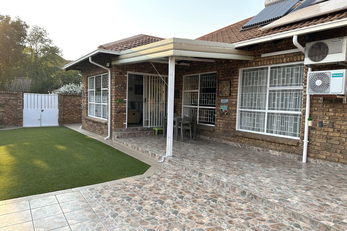 Rear view of the townhouse featuring a covered tiled patio, artificial lawn, brick exterior, and installed solar water heating system.