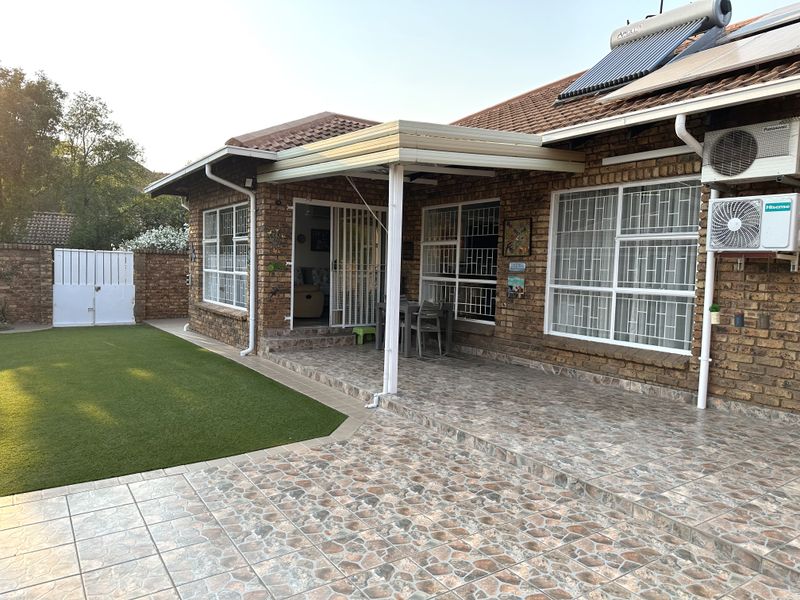 Rear view of the townhouse featuring a covered tiled patio, artificial lawn, brick exterior, and installed solar water heating system.