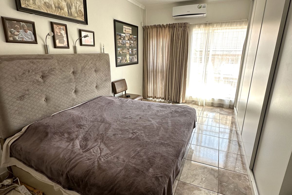 A bedroom featuring tiled flooring, built-in cupboards, and a wall-mounted split-system air conditioner, providing a functional and climate-controlled living space.