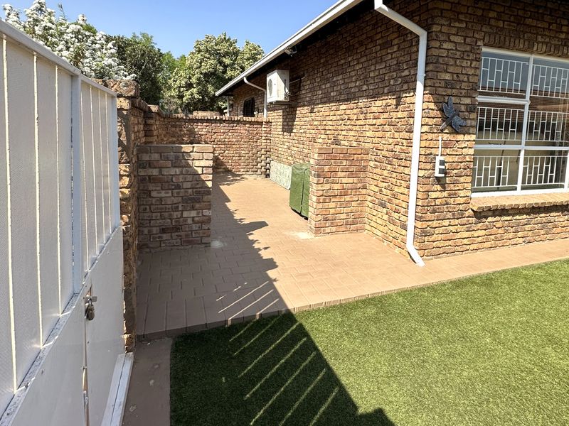 A private rear courtyard featuring a paved patio area, artificial lawn, and face brick exterior walls with security bars on the windows.