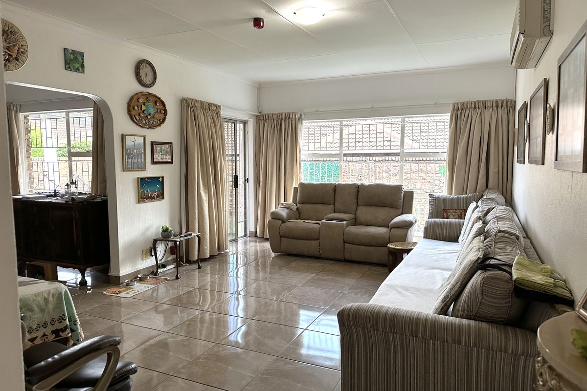 Spacious living room featuring large windows with security bars, tiled flooring, and a wall-mounted air conditioning unit, offering direct access to the exterior.