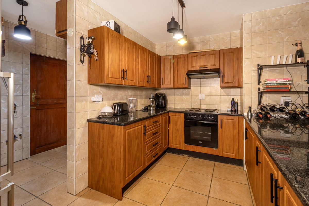 A functional kitchen featuring warm-toned wooden cabinetry, granite countertops, built-in oven, electric hob, and tiled finishes throughout.