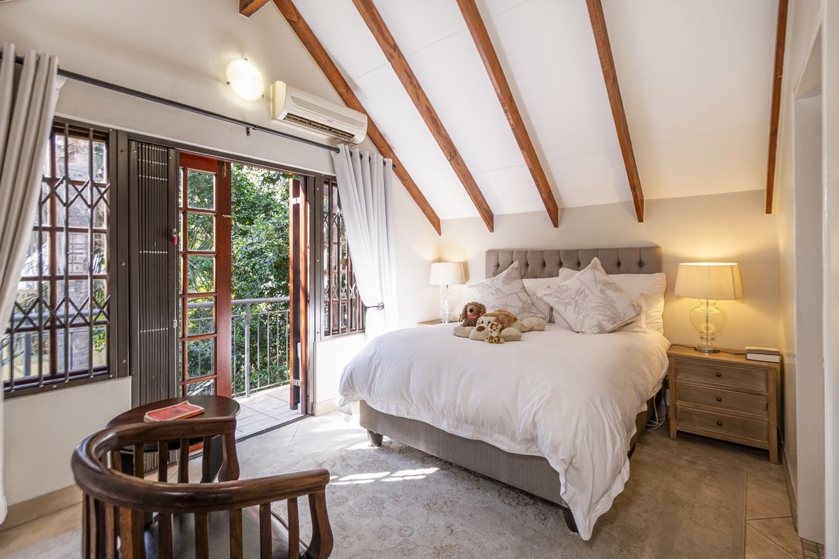 Spacious bedroom featuring exposed timber ceiling beams, split-system air conditioning, and direct access to a private balcony through timber-framed glass doors.