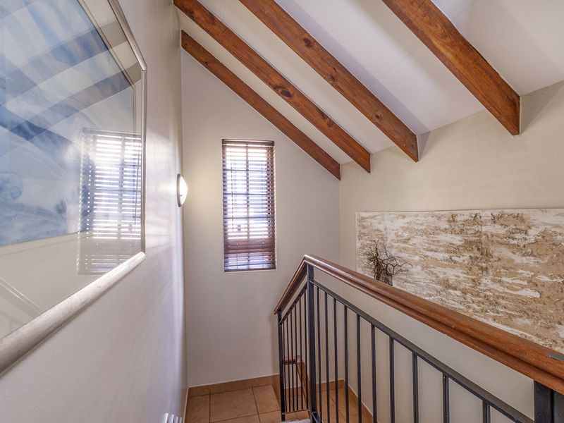 A bright hallway featuring exposed timber ceiling beams, a wrought iron balustrade with a timber handrail, and tiled flooring.