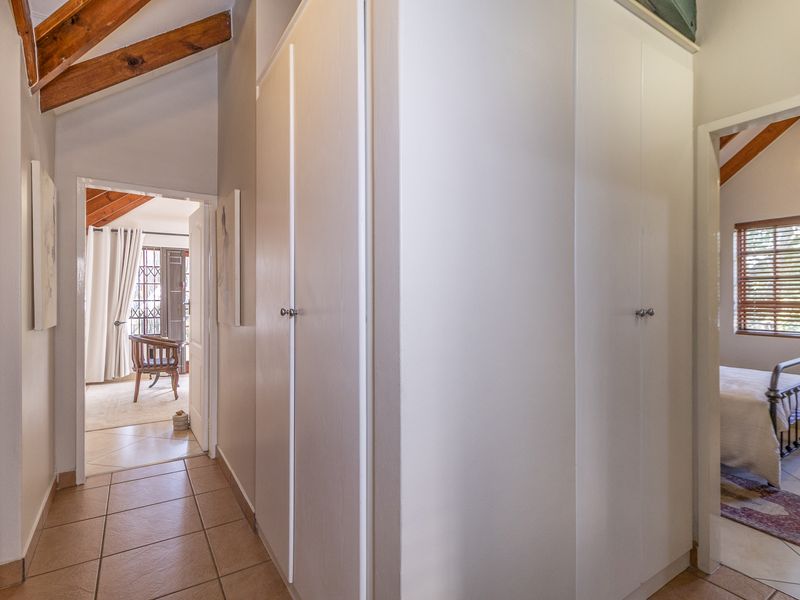 A bright hallway featuring built-in cupboards, exposed timber rafters, and tiled flooring, providing access to adjacent living and bedroom areas.