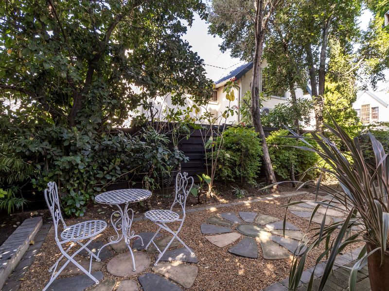 A private garden area featuring stone paving, gravel ground cover, and established trees, enclosed by timber boundary fencing.