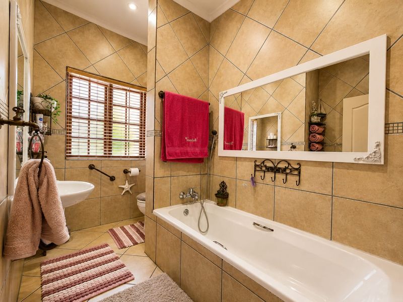 A functional bathroom featuring a built-in bathtub, wall-mounted basin, and neutral tiled finishes with wooden window blinds.