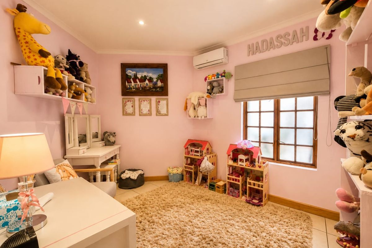A well-maintained bedroom featuring tiled flooring, recessed downlighting, an integrated air conditioning unit, and a timber-framed window with a fitted roman blind.
