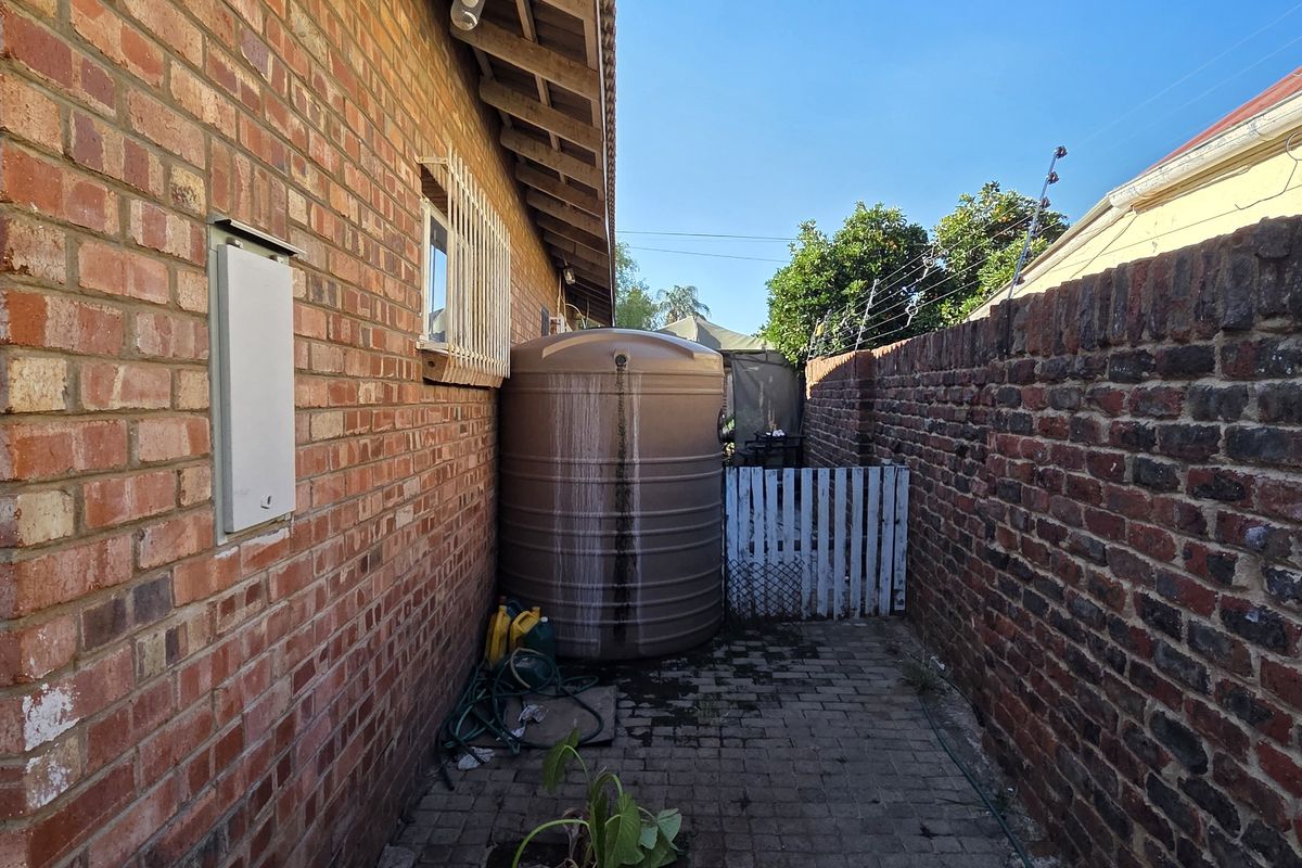 A narrow side passage featuring a brick boundary wall, paved flooring, and a large water storage tank with security fencing.