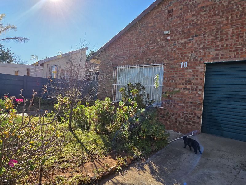 Front exterior view of a face brick house featuring a roller garage door, security bars on windows, and a front garden with boundary wall.