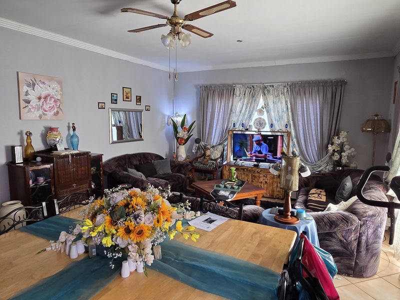 A spacious living room featuring tiled flooring, a ceiling fan, and decorative cornice detailing, providing a comfortable and functional family living area.