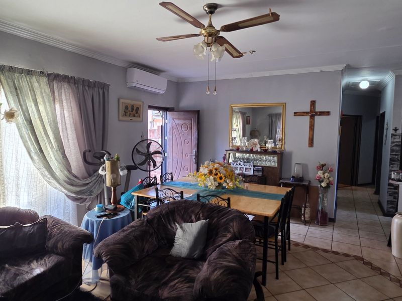 Open-plan living and dining area featuring tiled flooring, a ceiling fan, and a split-system air conditioner, flowing into an adjacent kitchen space.