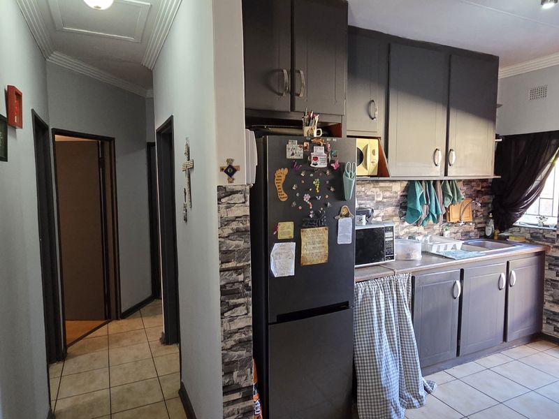A functional kitchen featuring built-in cabinetry, laminate countertops, and tiled flooring, adjacent to a hallway with access to other rooms.
