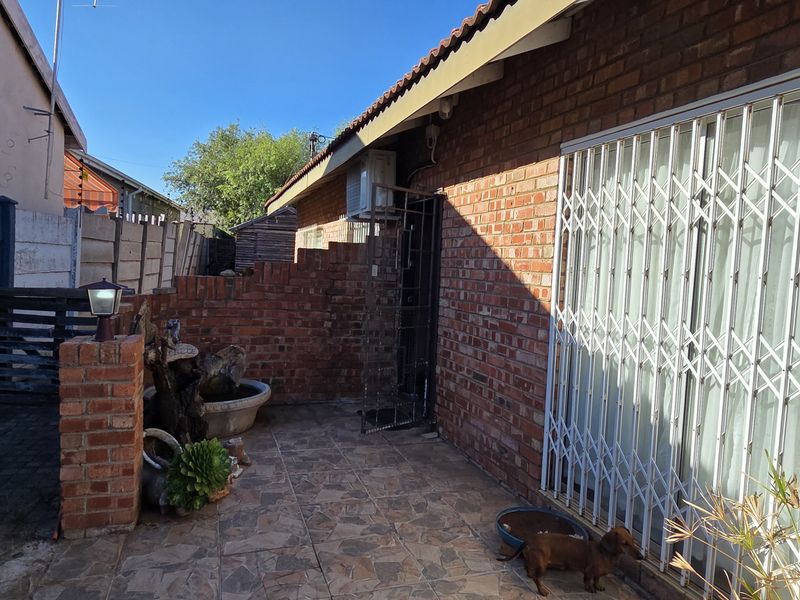 A rear exterior view of the house featuring a brick facade, tiled patio area, and security gate access.