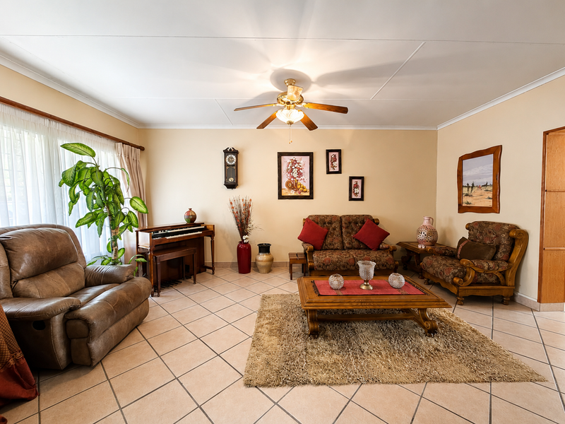 A spacious living room featuring neutral tiled flooring, a central ceiling fan, and coved ceiling detailing.