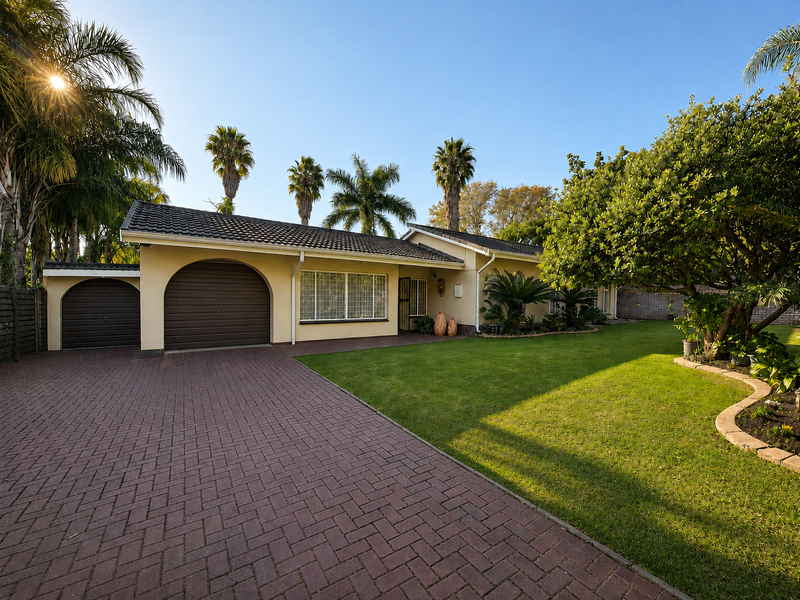 A well-maintained single-story home featuring a paved driveway, arched garage doors, and a neatly landscaped front garden with mature trees.