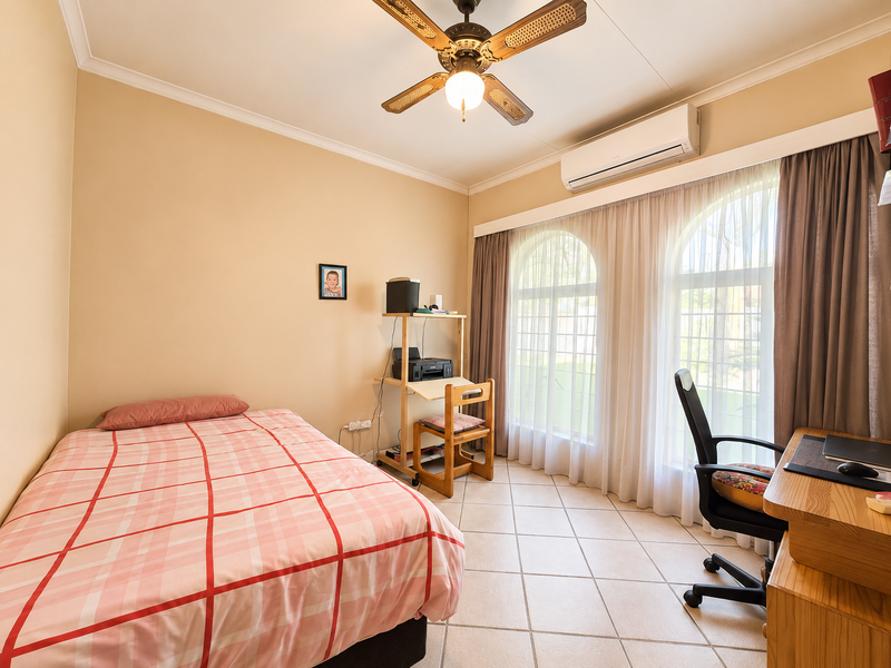 A well-lit bedroom featuring tiled flooring, a ceiling fan, split-system air conditioning, and large arched windows with curtains.