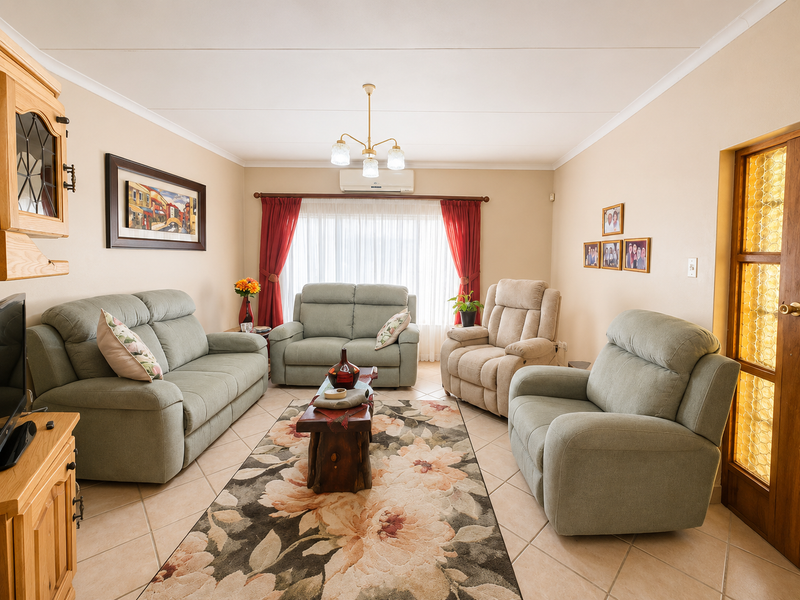 A comfortable living room featuring tiled flooring, a split-system air conditioner, and a classic timber-framed glass door, offering a functional and well-maintained space.