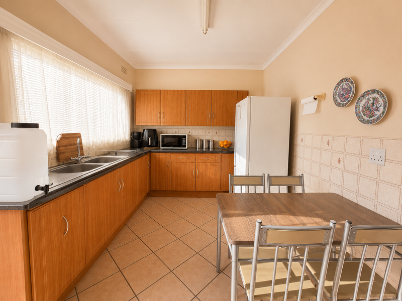 A functional kitchen featuring wood-look laminate cabinetry, a double stainless steel sink, tiled backsplash, and ceramic floor tiles with an integrated dining area.
