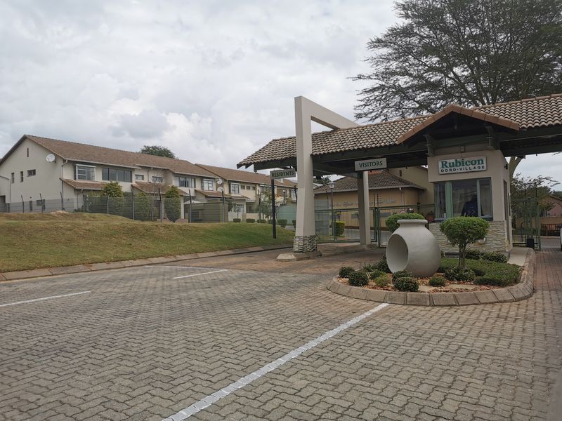 The entrance to Rubicon Retirement Village featuring a secure gatehouse, paved driveway, and well-maintained landscaped grounds.