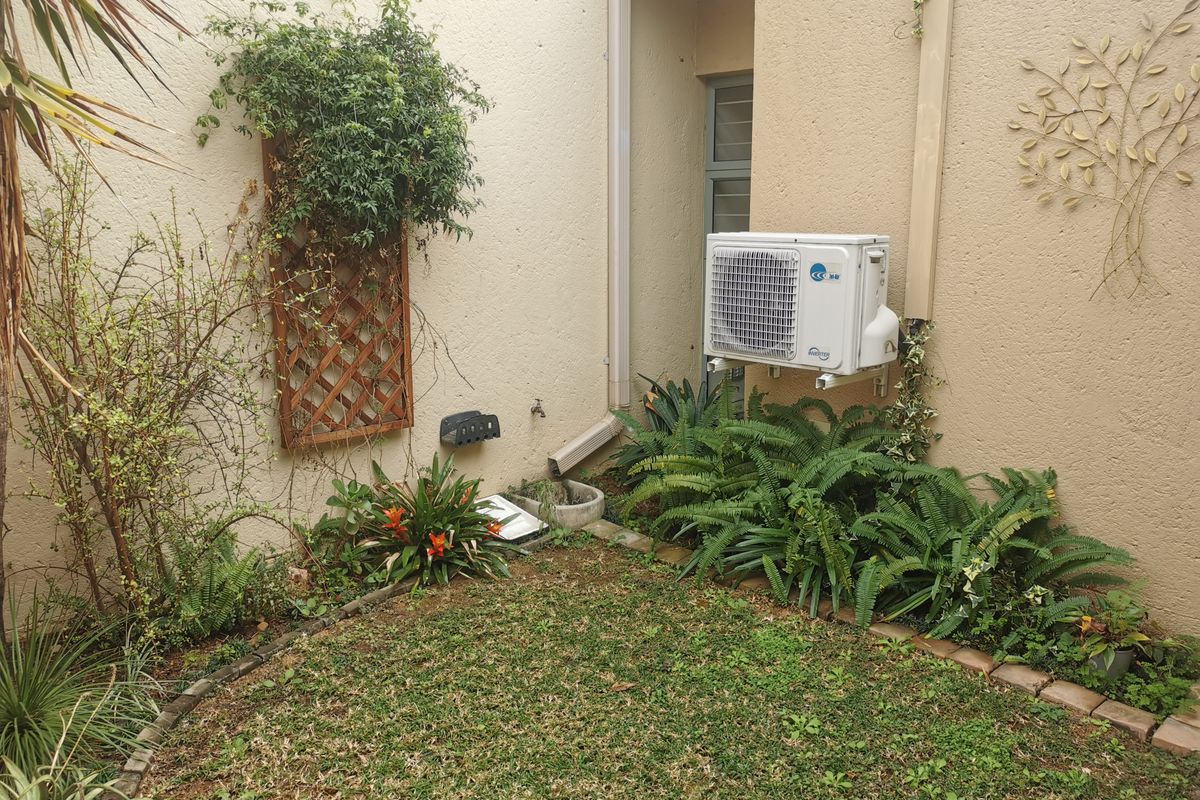 A private rear courtyard area featuring a small lawn, established garden beds, and a wall-mounted air conditioning condenser unit.