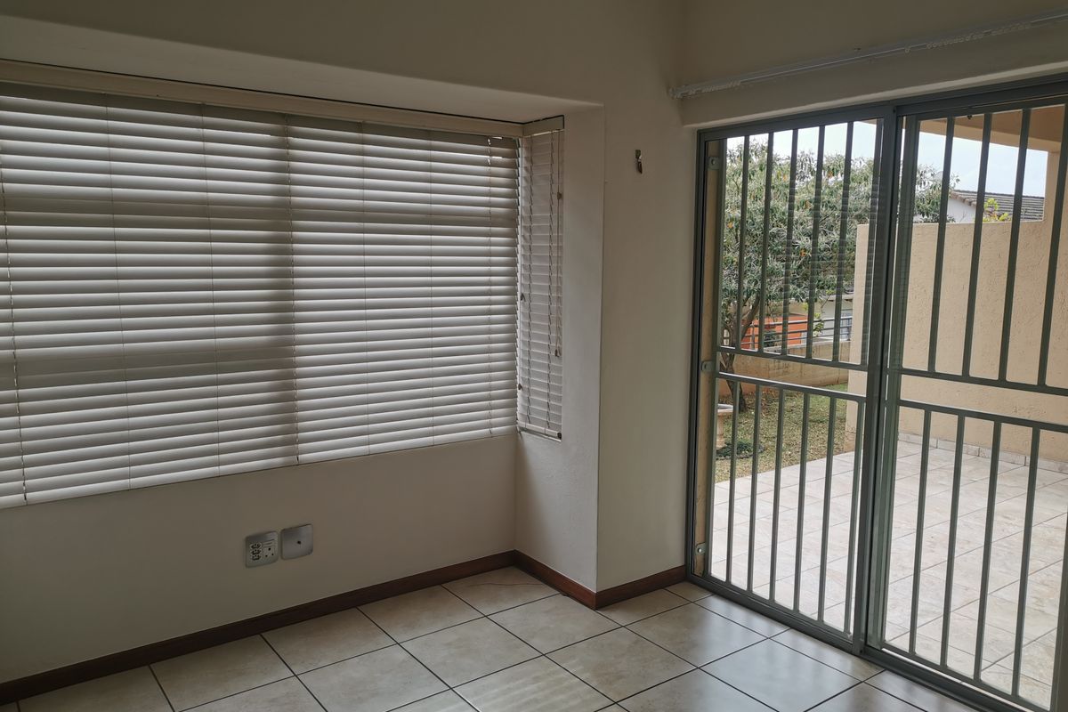 An empty living area featuring tiled flooring, venetian blinds, and a sliding glass door with a security gate leading to an outdoor patio.